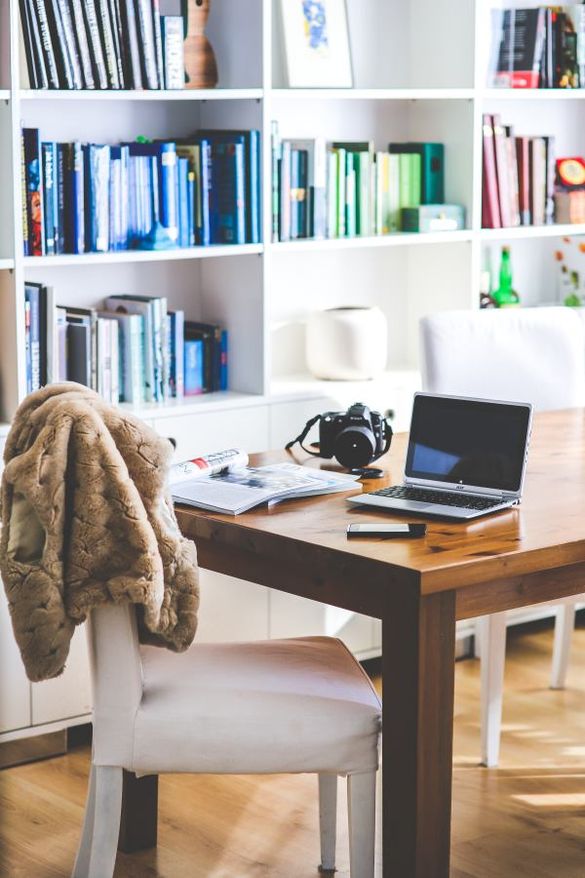 Dining table with laptop in a home environment and bookcase in the background